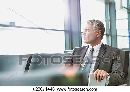 Stock Image - Mature businessman sitting and waiting for boarding in his gate at airport. Fotosearch