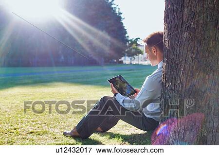 Mature businessman sitting under the tree while using digital tablet View Large Photo Image Stock Photo - Mature businessman sitting under the tree while using digital tablet. Fotosearch