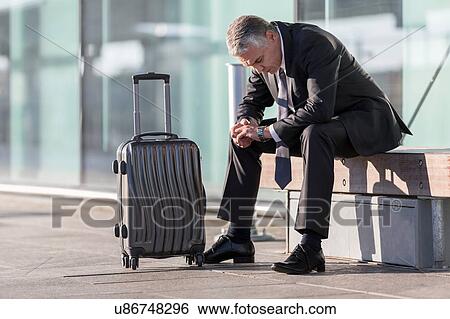 Stock Photograph - Mature businessman sitting while waiting in the airport. Fotosearch