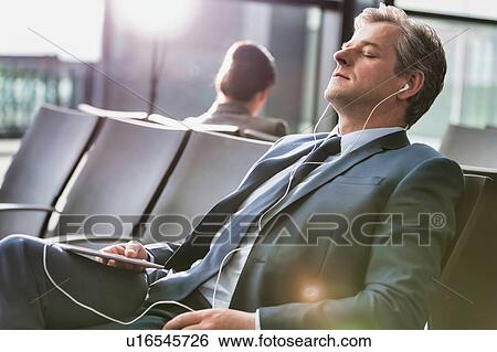 Mature businessman sleeping while listening to music with earphones on in airport with lens flare View Large Photo Image Stock Photograph - Mature businessman sleeping while listening to music with earphones on in airport with lens flare. Fotosearch