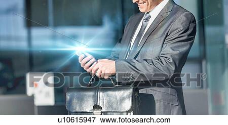 Stock Photo - Mature businessman smiling while using smartphone in airport. Fotosearch