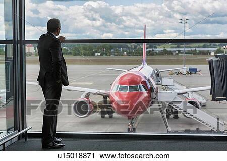 Stock Image - Mature businessman standing while looking on the plane in airport. Fotosearch