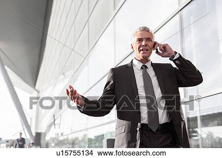 Picture - Mature businessman talking on smartphone in airport. Fotosearch