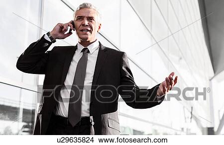 Picture - Mature businessman talking on smartphone in airport. Fotosearch
