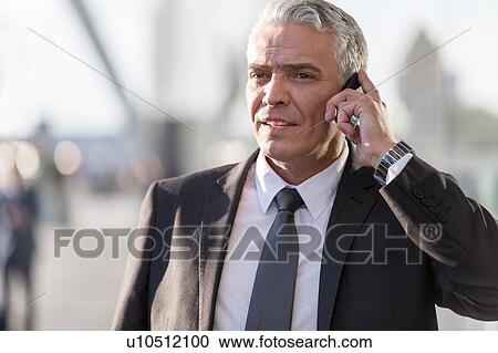 Stock Image - Mature businessman talking on smartphone in airport. Fotosearch