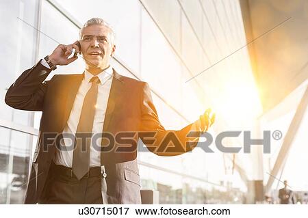 Stock Photo - Mature businessman talking on smartphone in airport. Fotosearch