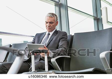 Stock Photograph - Mature businessman using digital tablet while sitting and waiting for boarding in his gate at airport. Fotosearch