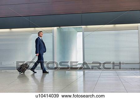 Stock Photo - Mature businessman walking with his suitcase in the airport. Fotosearch