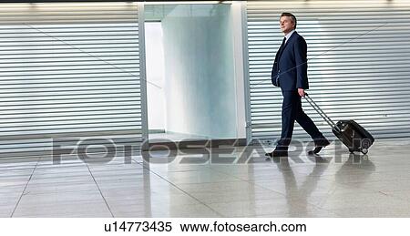 Stock Photography - Mature businessman walking with his suitcase in the airport. Fotosearch