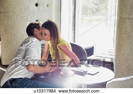Picture - Mature businessman whispering on attractive woman ear while sitting in lobby. Fotosearch