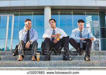 Stock Image - Mature businessmen sitting on stairs against office building after work. Fotosearch