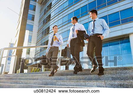 Picture - Mature businessmen talking while walking downstairs against office building after work. Fotosearch