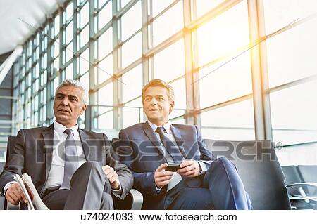 Stock Image - Mature businessmen talking while sitting and waiting for boarding in airport . Fotosearch