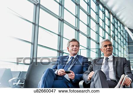 Stock Photo - Mature businessmen talking while sitting and waiting for boarding in airport . Fotosearch