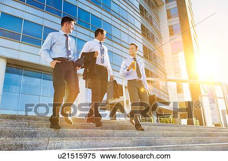 Stock Photography - Mature businessmen talking while walking downstairs against office building after work. Fotosearch
