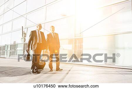 Stock Image - Mature businessmen walking while talking in the airport. Fotosearch