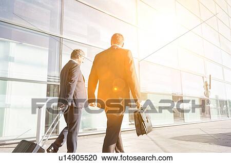 Stock Image - Mature businessmen walking while talking in the airport. Fotosearch