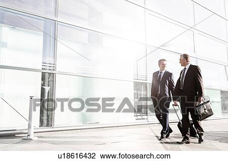 Stock Image - Mature businessmen walking while talking in the airport. Fotosearch