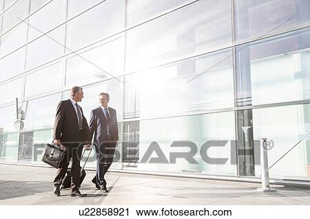 Stock Image - Mature businessmen walking while talking in the airport. Fotosearch
