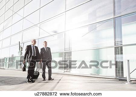 Stock Image - Mature businessmen walking while talking in the airport. Fotosearch