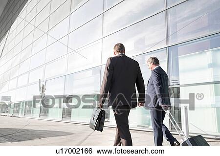 Stock Photograph - Mature businessmen walking while talking in the airport. Fotosearch