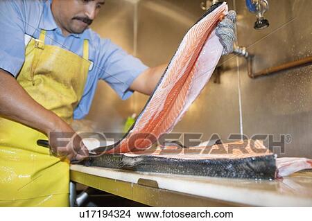 Picture - Mature fishmonger slicing salmon fish on table. Fotosearch