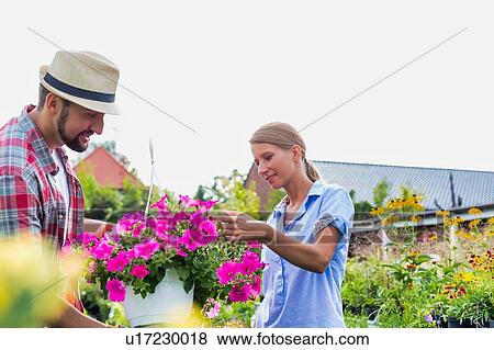 Stock Photo - Mature gardener showing flowers on pot to woman buyer in shop. Fotosearch