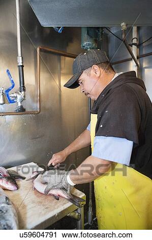 Stock Image - Mature male fishmonger cutting fish on table. Fotosearch