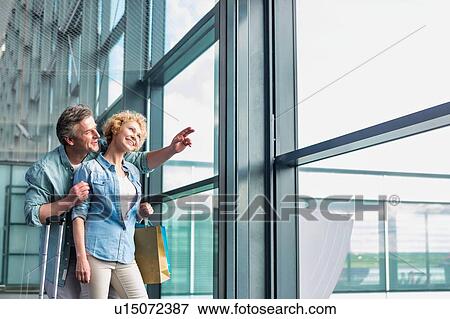 Mature man hugging his wife from behind while looking through the window in airport View Large Photo Image Stock Photo - Mature man hugging his wife from behind while looking through the window in airport. Fotosearch