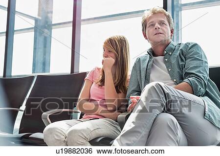 Stock Photograph - Mature man sitting with his daughter while waiting for their flight in airport. Fotosearch