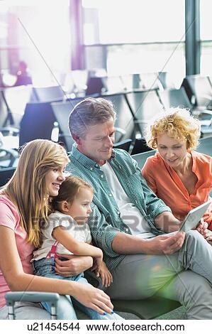 Picture - Mature man using digital tablet while his wife and daughter looking in airport. Fotosearch