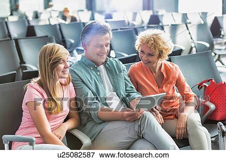 Stock Photo - Mature man using digital tablet while his wife and daughter looking in airport. Fotosearch