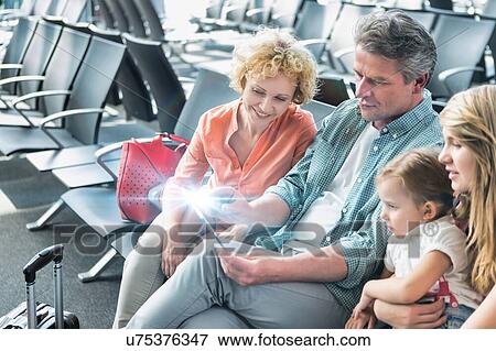 Stock Photo - Mature man using digital tablet while his wife and daughter looking in airport. Fotosearch