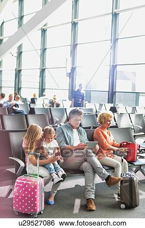 Stock Photograph - Mature man using digital tablet while his wife and daughter looking in airport. Fotosearch