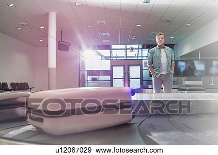 Stock Photo - Mature man waiting for his suit case on baggage claiming area in airport. Fotosearch
