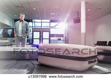Stock Photo - Mature man waiting for his suit case on baggage claiming area in airport. Fotosearch