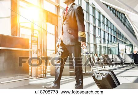 Stock Photo - Mature pilot walking to enter the plane in boarding gate at airport. Fotosearch