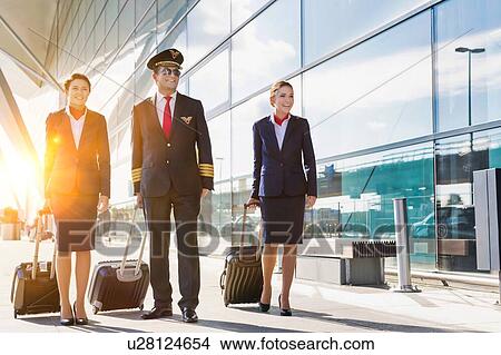 Picture - Mature pilot with young beautiful flight attendants walking in airport. Fotosearch