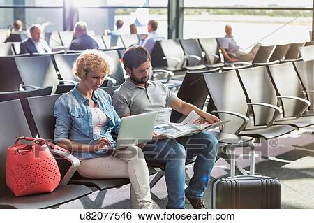Stock Photograph - Mature woman working on her laptop, husband is reading newspaper while waiting for boarding in airport. Fotosearch