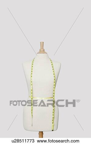 Stock Image - Measuring tape on dressmakers model over colored background. Fotosearch