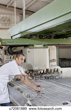 Stock Photo - Mid adult industrial worker concentrating while operating machinery in factory. Fotosearch