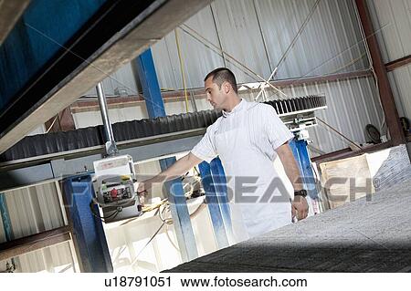 Stock Image - Mid adult industrial worker using machinery in factory. Fotosearch