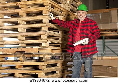 Middle aged working standing in front of wooden pallets View Large Photo Image Stock Image - Middle aged working standing in front of wooden pallets. Fotosearch