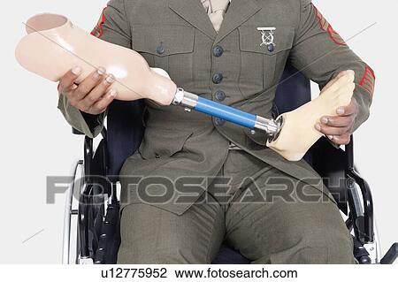 Stock Image - Midsection of a US military officer holding prosthesis leg as he sits in wheelchair. Fotosearch