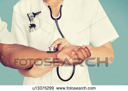 Stock Photo - Midsection of nurse checking the pulse of a patient through stethoscope. Fotosearch