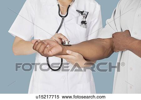 Stock Photography - Midsection of nurse checking the pulse of a patient through stethoscope. Fotosearch