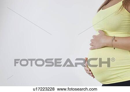 Midsection of young pregnant woman against white background View Large Photo Image Stock Photo - Midsection of young pregnant woman against white background. Fotosearch