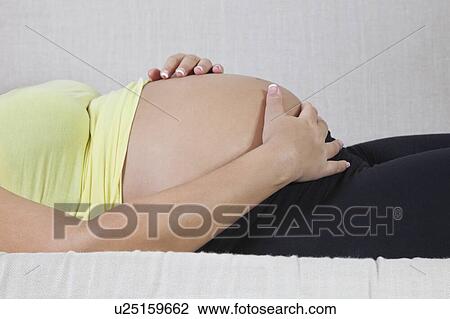 Midsection of young pregnant woman with hands on stomach relaxing at home View Large Photo Image Stock Image - Midsection of young pregnant woman with hands on stomach relaxing at home. Fotosearch