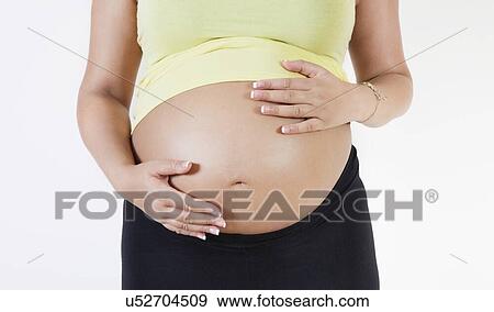 Midsection of young pregnant woman with hands on stomach against white background View Large Photo Image Stock Photo - Midsection of young pregnant woman with hands on stomach against white background. Fotosearch
