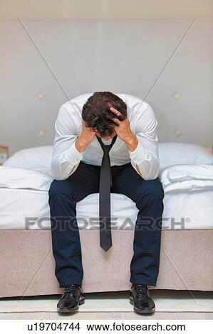 Overworked and stressed businessman sitting on the bed View Large Photo Image Picture - Overworked and stressed businessman sitting on the bed. Fotosearch